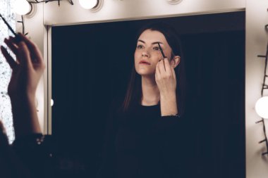 Makyaj sanatçısı kadın makyaj fırçası kullanıyor. Kadın aynaya bakıyor..