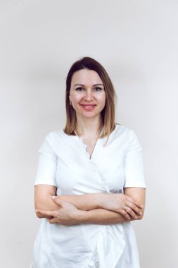 Güzellik uzmanı kameraya gülümsedi, kollarını kavuşturdu. Mesaj ya da logo için yer var. İzole edilmiş beyaz bir arka planda beyaz bir önlük içinde güzel bir bayan doktor..