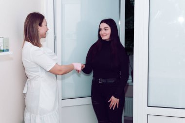 A cosmetologist in a white medical coat opened the door to wait for the client. A doctor in a white coat meets a client at the entrance to his office.