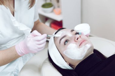 Beyaz tıbbi önlüklü bir kozmetik bilimci estetik ameliyattan önce bir müşteriye makyaj bandı takıyor. Beyaz önlüklü bir doktor müşterisini yüz temizleme için hazırlar..