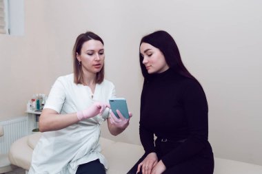 Beyaz önlüklü bir kozmetikçi müşteriye açıklıyor. Mutlu güzellik uzmanı ve müşteri kanepede konuşuyor. Doktor güzellik uzmanı ve müvekkil, tedavi sonuçlarını telefondan izliyorlar..
