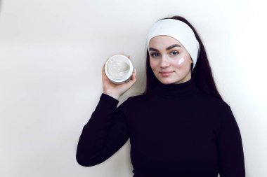 Siyah kazaklı ve kafasında beyaz bir bandaj olan bir kadın güzellik uzmanında elinde bir kavanoz krema tutuyor. Yanağında krem lekesi olan güzel bir kadın. Güzellik tedavi konsepti