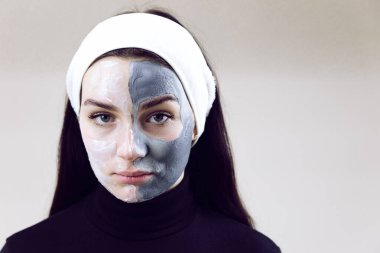 Siyah giyinmiş ve beyaz bantlı bir kadın güzellik uzmanının randevusunda. Yüzünde kozmetik maske olan güzel bir kadın. Gri arkaplanda metin için yer alan kozmetik maske yapan kadın