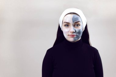 Siyah giyinmiş ve beyaz bantlı bir kadın güzellik uzmanının randevusunda. Yüzünde kozmetik maske olan güzel bir kadın. Gri arkaplanda metin için yer alan kozmetik maske yapan kadın