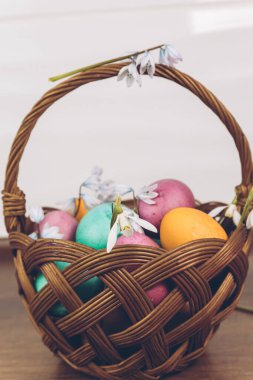 Paskalya geçmişi. Sepette paskalya yumurtası. Sarı, yeşil ve mor yumurtalarla süslü bir Paskalya sepeti ahşap bir masada duruyor..