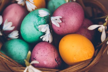 Paskalya geçmişi. Sepette paskalya yumurtası. Sarı, yeşil ve mor yumurtalarla süslü bir Paskalya sepeti ahşap bir masada duruyor..