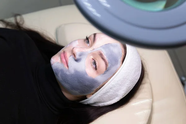 Woman having cosmetic face mask view through beauty lamp charm. Cosmetological procedure in a beauty salon. Facial skin care. Beautiful woman with cosmetic facial mask in the spa salon.