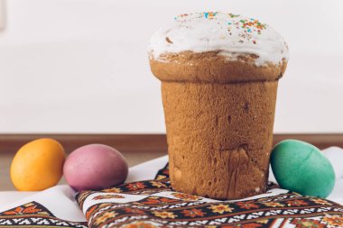 Paskalya yumurtaları ve paskalya pastası nakışlı bir havluda. Tahta bir masa üzerinde Ukrayna işlemeli gömlek ve Paskalya pastası ve farklı renklerde Paskalya yumurtaları - sarı, yeşil ve mor yumurtalar.