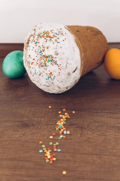 Easter eggs and cake with scattered sweets. Easter cake with scattered sprinkles on a wooden table, and Easter eggs of different colors - yellow eggs, green and purple eggs.