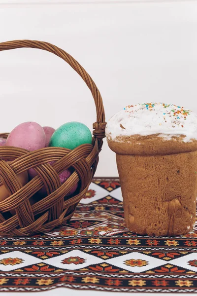 Easter eggs and Easter cake on an embroidered towel. Ukrainian embroidered shirt and Easter cake on a wooden table with Easter eggs of different colors - yellow eggs, green and purple eggs in a basket.