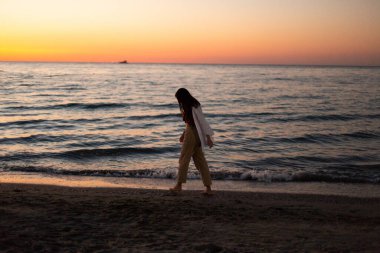 Beyaz elbiseli ince bir kız denizin arka planında sahil boyunca yürür. Şafakta sportif bir kız denizin seti boyunca koşar. Denizde şafak.