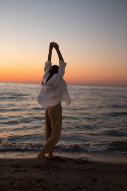 Beyaz elbiseli ince bir kız denizin arka planında sahil boyunca yürür. Şafakta sportif bir kız denizin seti boyunca koşar. Denizde şafak.