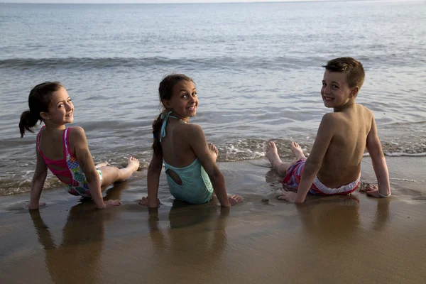 Tre bambini preadolescenti carini seduti in acqua sulla spiaggia — Foto Stock