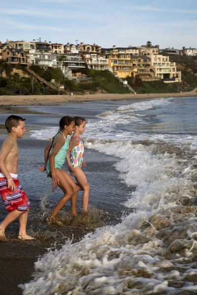 Preteen children playing at the beach running into waves — Stock Photo, Image