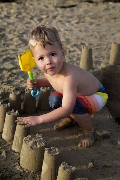 Brown eyed blond pojke spelar i ett sandslott på stranden — Stockfoto