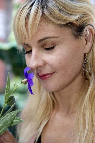 Blond vrouwelijke portret ruiken paarse flowere met haar ogen clos — Stockfoto