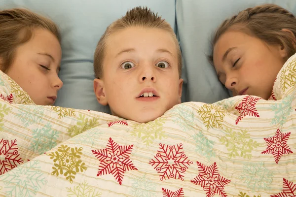 Roliga uttryck på pojkar ansikte mellan två kusiner i sängen — Stockfoto