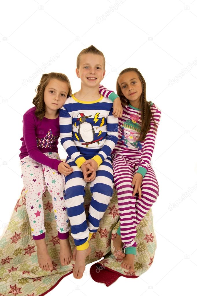 Three kids in colorful pajamas sitting on a blanket