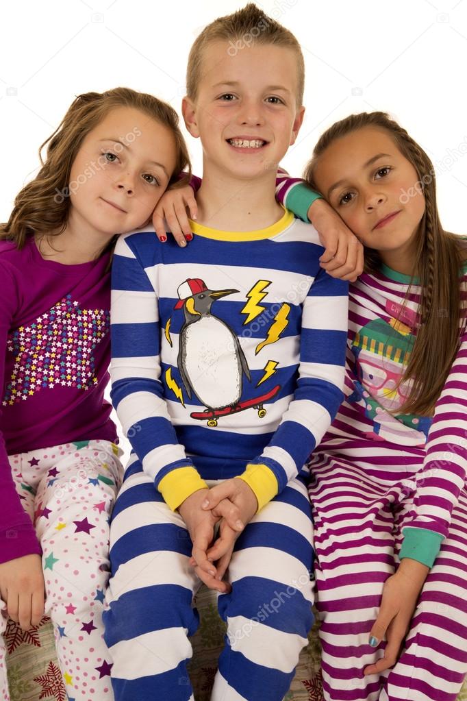 Three children wearing winter pajamas sitting smiling happy