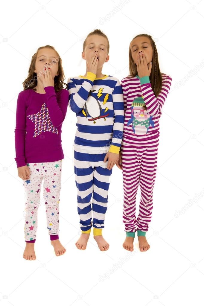 Three adorable children wearing colorful winter pajamas yawning