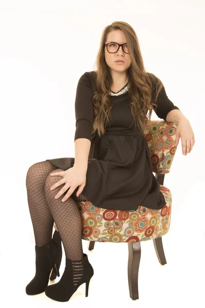 Female brunette model wearing a black dress sitting in a floral chair — Stock Photo, Image