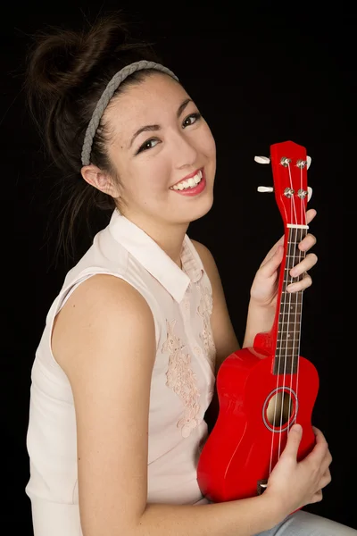 Atractiva chica adolescente sosteniendo un ukelele rojo sonriendo — Foto de Stock