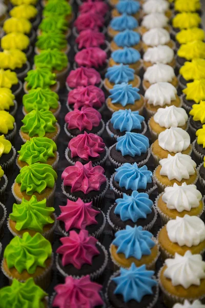 Mais de três dúzias de cupcakes coloridos em linhas verticais Fotografia De Stock