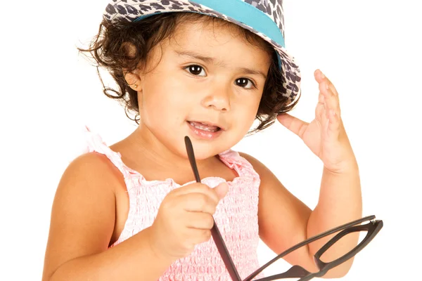 Cute Hispanic toddler girl wearing hat playing with glasses — Stock Photo, Image