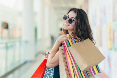 Markette yürürken renkli alışveriş torbaları taşıyan şık siyah elbiseli neşeli bir bayan. Çekici esmer, alışveriş merkezinden alışveriş yaptıktan sonra tatmin olmuş görünüyor..
