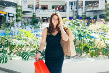 Markette yürürken renkli alışveriş torbaları taşıyan şık siyah elbiseli neşeli bir bayan. Çekici esmer, alışveriş merkezinden alışveriş yaptıktan sonra tatmin olmuş görünüyor..
