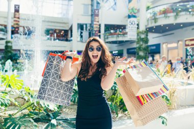 Markette yürürken renkli alışveriş torbaları taşıyan şık siyah elbiseli neşeli bir bayan. Çekici esmer, alışveriş merkezinden alışveriş yaptıktan sonra tatmin olmuş görünüyor..