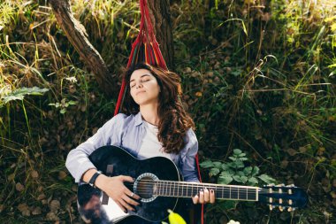Parktaki ağaçların ortasında bir hamakta dinlenen güzel bir kız. Elinde gitarıyla.