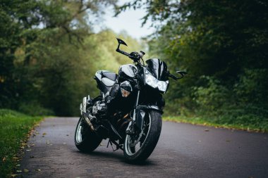 Genç bir çift, siyah spor bir motosikletin yanındaki adam ve kız, siyah deri elbiseli, ormanda yolda.