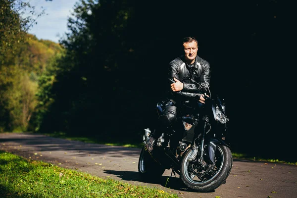 Mężczyzna Czarnym Motocyklu Sportowym Czarnych Skórzanych Ubraniach Drodze Lesie — Zdjęcie stockowe
