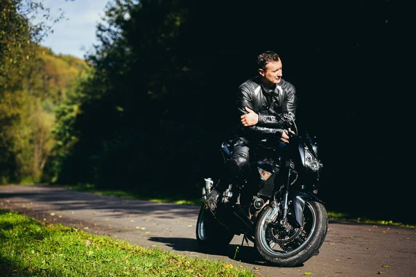 一个骑着黑色摩托车 身穿黑色皮衣的男子在林子里的路上 — 图库照片