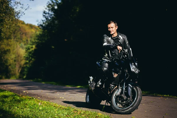 Mężczyzna Czarnym Motocyklu Sportowym Czarnych Skórzanych Ubraniach Drodze Lesie — Zdjęcie stockowe