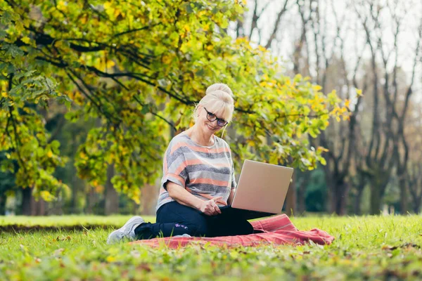 Oudere Vrouw Rustend Het Park Zittend Het Gras Met Telefoon — Stockfoto