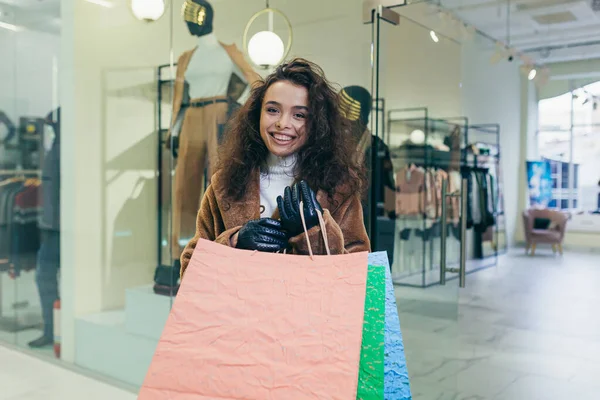 若い美しい女性は 商品と色の袋を保持店を残し 彼らの購入に満足しているようだ — ストック写真