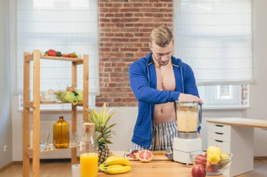 Erkek sporcu mutfakta meyve salatası ve taze meyve suyu hazırlıyor.