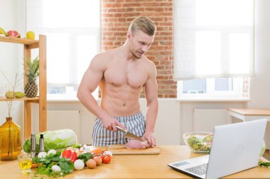 Sporcu adam mutfakta yemek pişirir, sebze ve çeşitli etleri yemek için kullanır, çevrimiçi aşçılık dersleri izler.