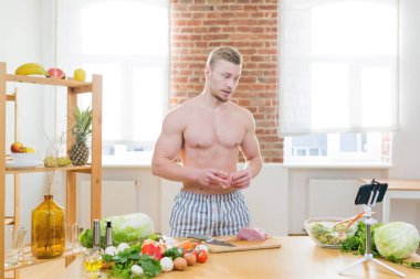 Sporcu adam mutfakta yemek pişirir, sebze ve çeşitli etleri yemek için kullanır, çevrimiçi aşçılık dersleri izler.