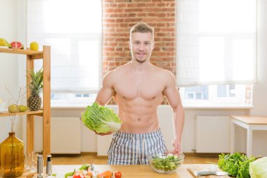 Sporcu adam mutfakta yemek pişirir, sebze ve çeşitli etleri yemek için kullanır.