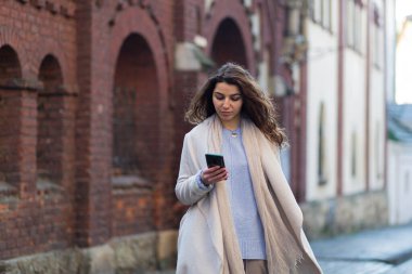 Yeni bir şehirde elinde telefon ve bavuluyla yürüyen güzel esmer bir kadın, bir turist yeni şehirler keşfediyor.