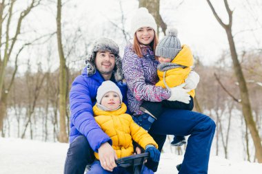 Mutlu bir aile kış parkında birlikte yürüyor. İki yetişkin adam, kadın ve iki çocuk.