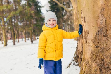 Küçük çocuk kışın ailesiyle parkta yürüyüş yapıyor, eğleniyor ve karın tadını çıkarıyor.