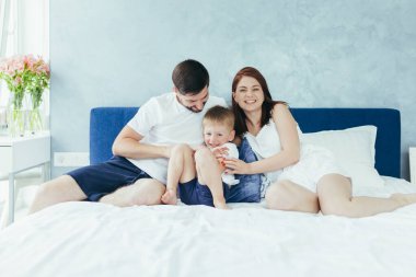Genç bir aile kadını, koca ve oğlu sabah büyük bir yatak odasında birlikte eğleniyorlar.