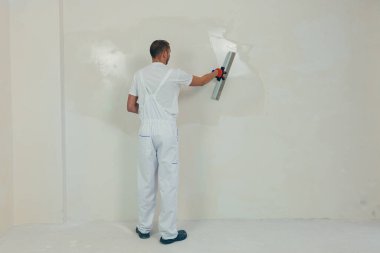 Bir işçi duvarı spatulayla kaplıyor ve çimento karışımı solüsyonu uyguluyor. Tamirci alçıpanı alçıpan üzerine serer..