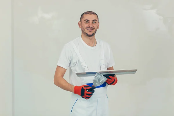 A man worker plasters the wall with a spatula and applies a cement mix solution. The repairman lays the plaster on the drywall.