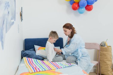 Hasta bir çocuğu evinde muayene eden çocuk doktoru hastayı eğlendirmeye ve neşelendirmeye çalışıyor.