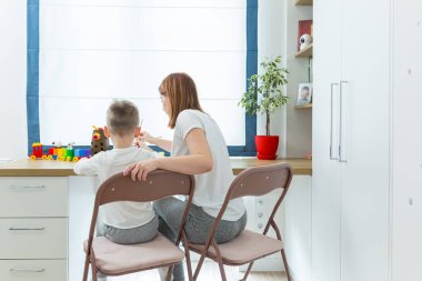 Genç anne, küçük oğluna resim çizmeyi öğretiyor, evde çocuk odasında, birlikte eğleniyor.